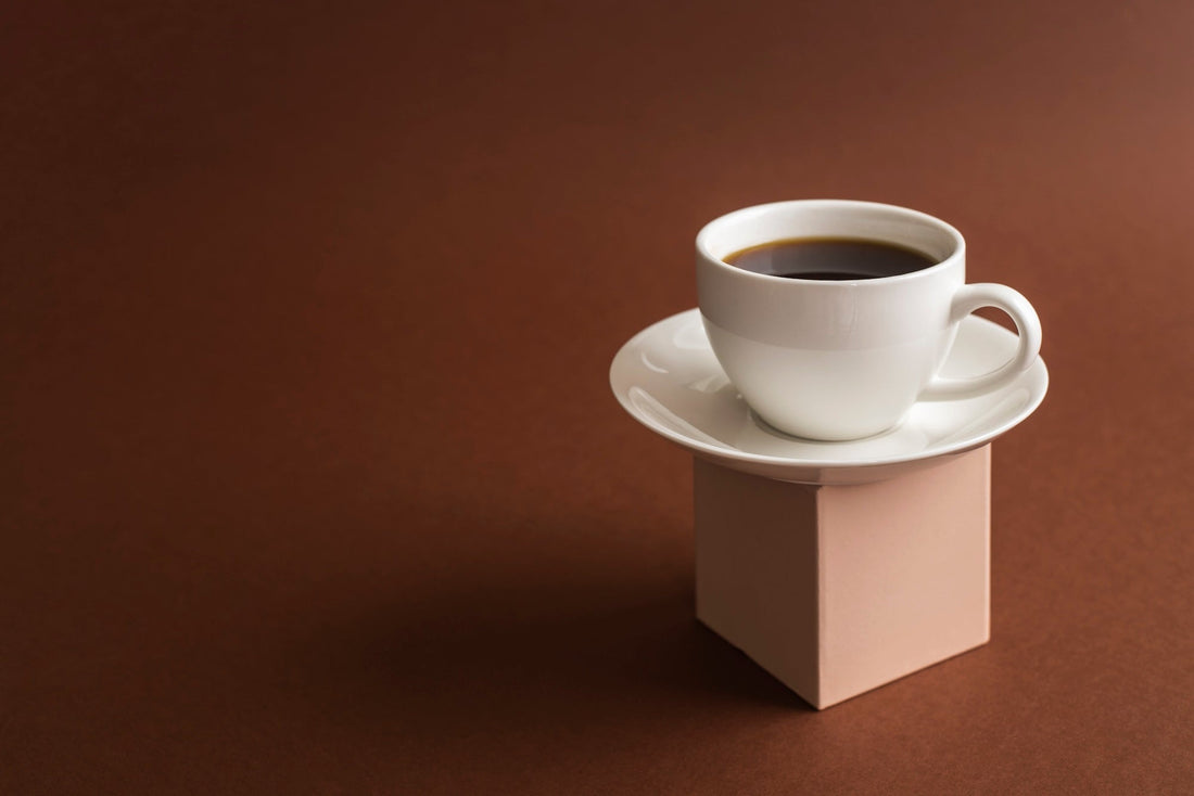 a cup of coffee on a white dish in front of a brown background