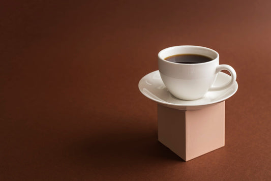 a cup of coffee on a white dish in front of a brown background