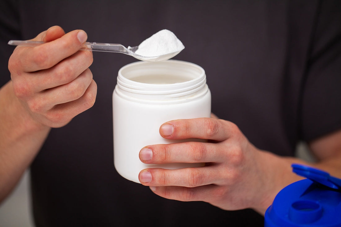 male hands holding a white tub with a spoon full of white creatine powder