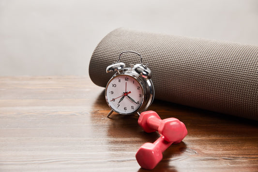a silver alarm clock next to small red dumbbells on a wooden floor