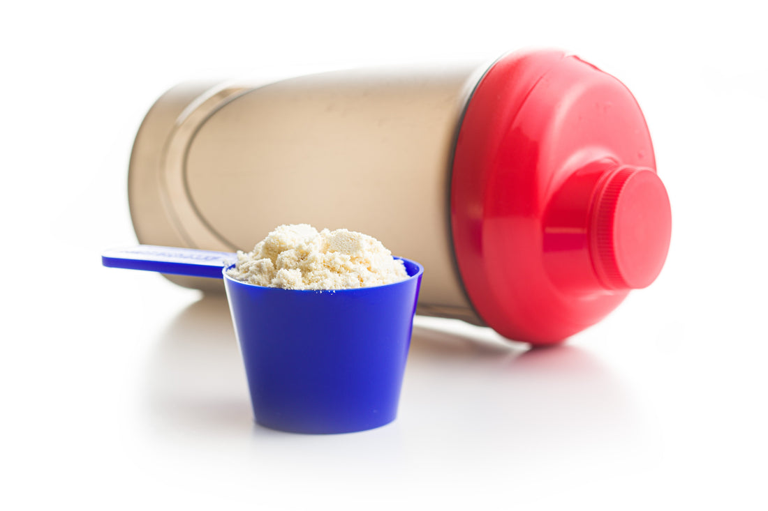 a red shaker cup next to a blue scooper with whey protein powder