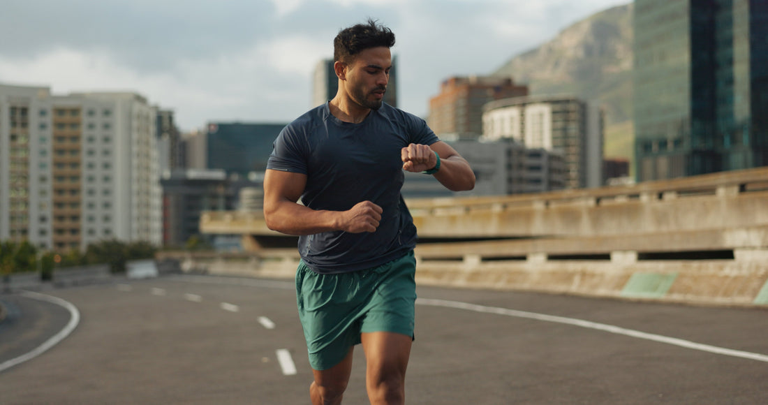 a man running in shorts on a road while looking at his watch