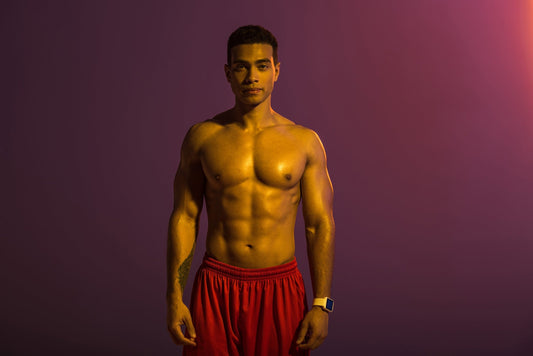 a muscular man in red shorts in front of a purple background
