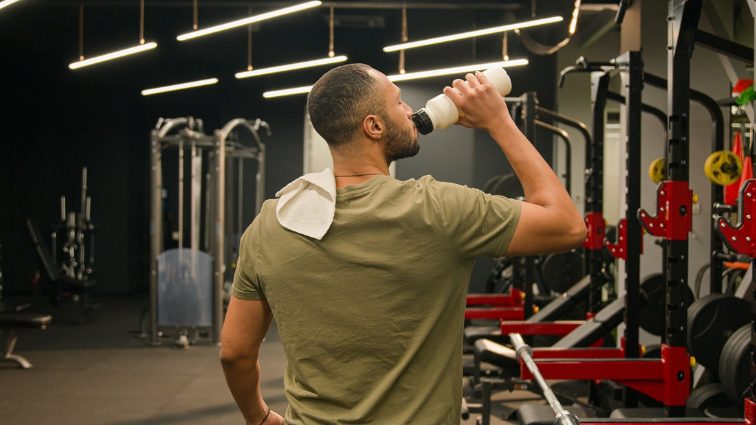 a man in a green shirt drinking out of a bottle in front of a gym backdrop