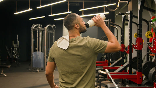a man in a green shirt drinking out of a bottle in front of a gym backdrop