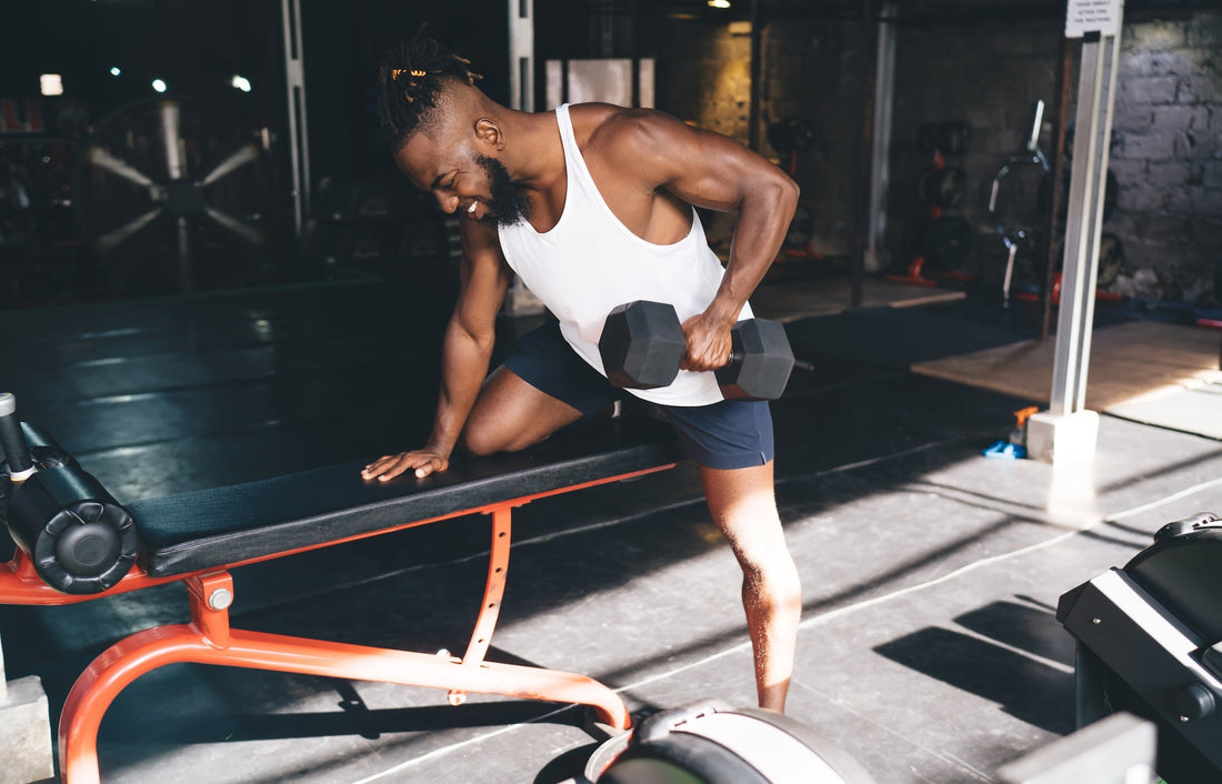 a man doing a workout with a dumbbell in a white tank top and black shorts