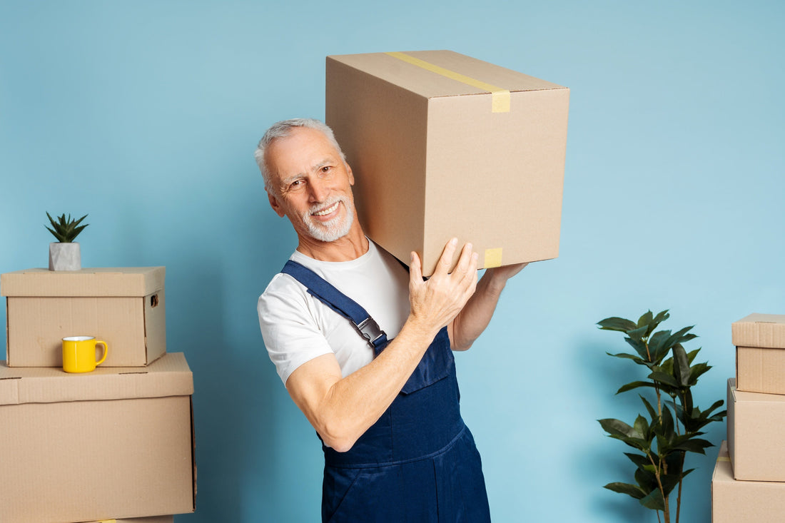 a man in blue overall lifting a heavy cardboard box in front of a blue wall