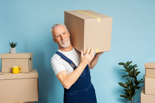 a man in blue overall lifting a heavy cardboard box in front of a blue wall