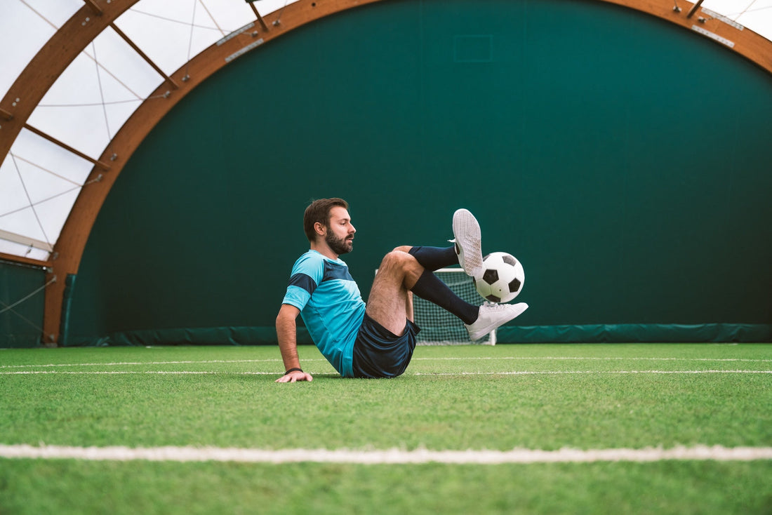 a soccer player sitting on a field and freestyling with the ball