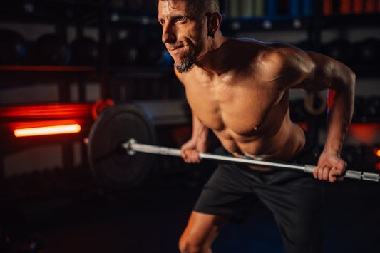 a shirtless bodybuilder doing rows with a barbell with a red light in the background