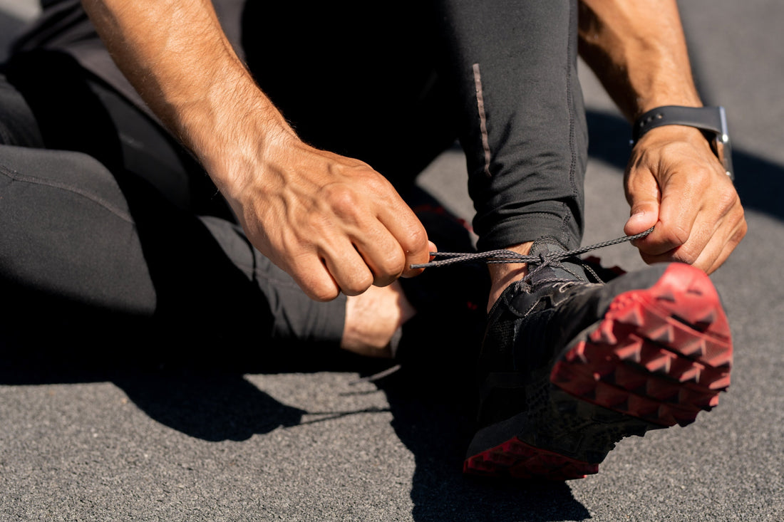 a close up of a runner in black pants and black and red shoes tying his laces