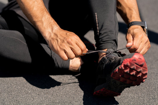 a close up of a runner in black pants and black and red shoes tying his laces
