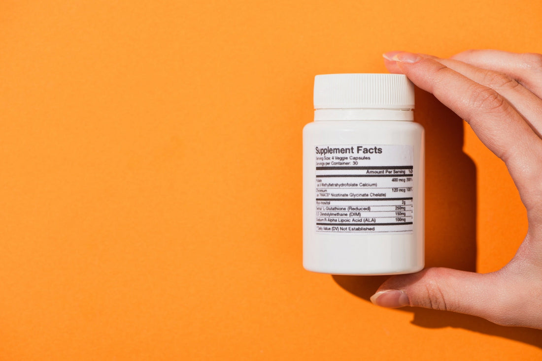 a hand holding a jar of vitamins with a supplement facts label in front of an orange background