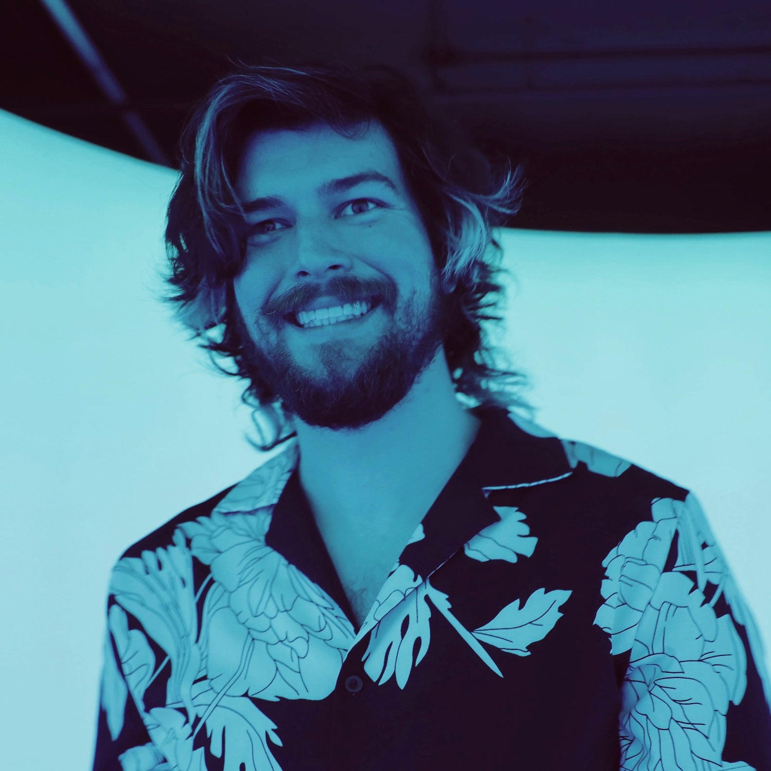 Man with a beard wearing a floral shirt in a colored photo room with blue tint